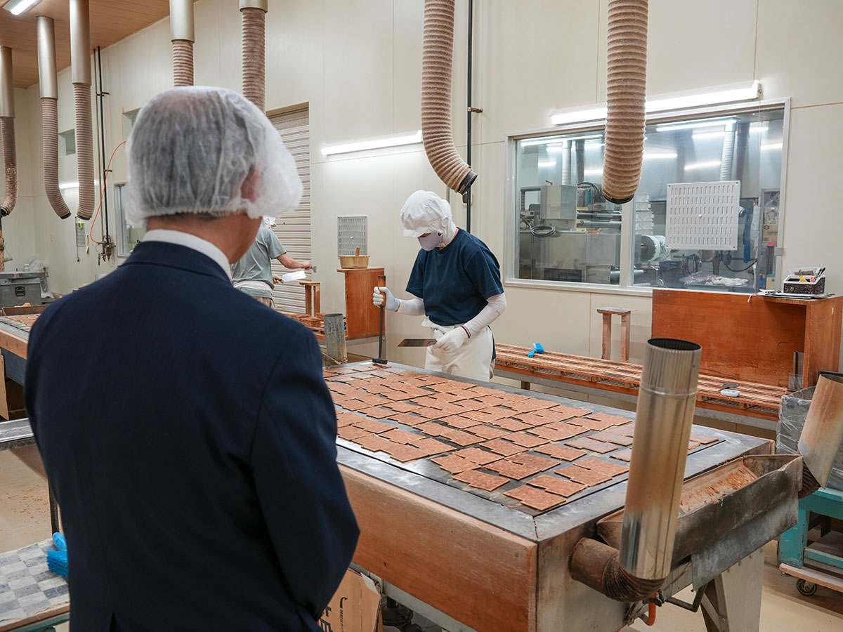 瓦せんべい製造工場内で作業中の様子を見つめる田村氏
